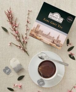Ahmad Earl Grey thee voor horeca, doos met 100 theezakjes naast kopje thee en bloemen op tafel.