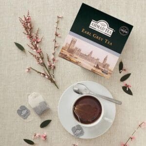 Ahmad Earl Grey thee voor horeca, doos met 100 theezakjes naast kopje thee en bloemen op tafel.
