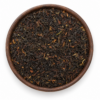 Darjeeling zwarte thee als losse droge thee in een rond houten bakje op witte achtergrond