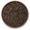 Pu Erh thee als losse droge thee in een rond houten bakje op witte achtergrond